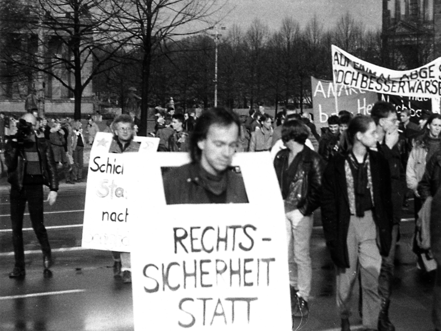 Demonstranten mit Transparenten und Plakaten. Vorne im Bild trägt ein Mann ein Transparent, worauf der Anfang des Schriftzuges "Rechtssicherheit statt" lesbar ist.